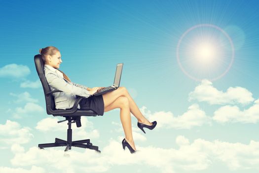 Beautiful businesswoman in suit sitting on office chair and holding open laptop, leaning back, smiling