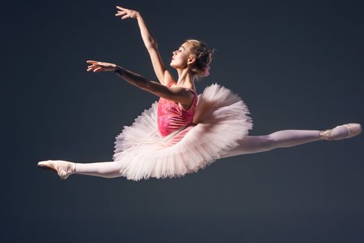 Beautiful female ballet dancer on a grey background. Ballerina is wearing  pink tutu and pointe shoes
