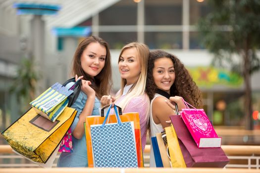shopping, sale, happy people and tourism concept - three beautiful girls with shopping bags in mall