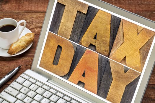 tax day in letterpress wood type - a message on a laptop screen with cup of coffee