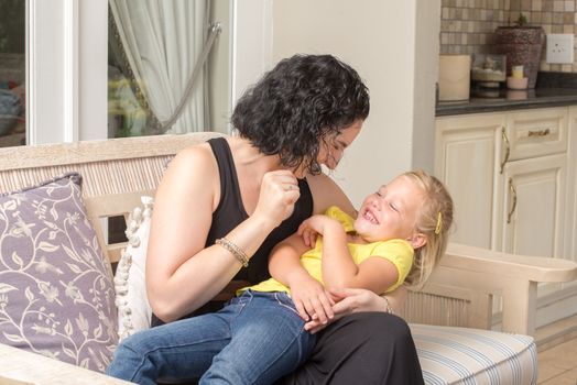 A young mother and her daughter are playing and having fun while sitting on a couch outside on the porch of their home.