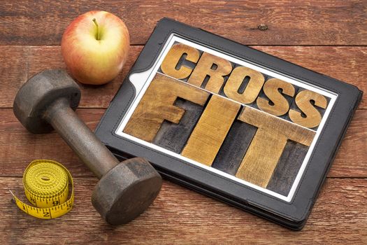 crossfit word abstract - text in letterpress wood type on a digital tablet with dumbbell and tape measure - fitness concept