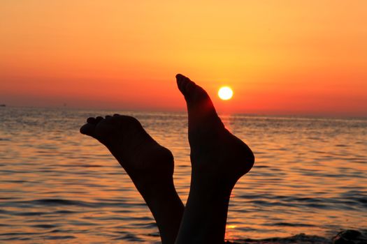 Naked woman legs and evening beach on the sunset