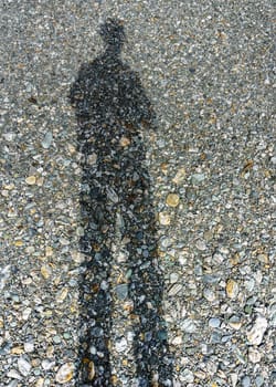 Stretched man shadow on stone covered ground, dry river bed.