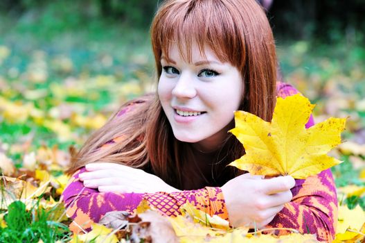 happy redheaded girl laying on the leaves in autumn forest 