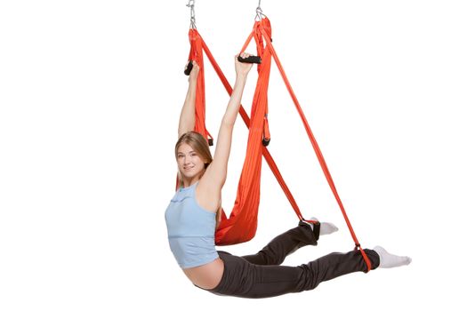 Young woman upside down doing anti-gravity aerial yoga in red hammock on a seamless white background.