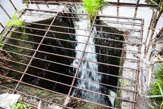 Water flowing into the spillway with metal grate on the dam. Close up.