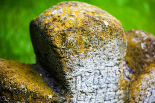 Old moss-grown stone cross with engraved Old Church Slavonic inscriptions. Kyiv, Ukraine. Close up.