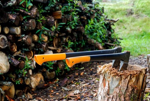 Two ax stuck in the trunk on the background of firewood.