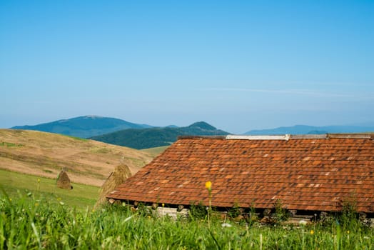 Landscape in the Ukrainian Carpathian Mountains. Wooden house with orange tiled roof in the foreground,