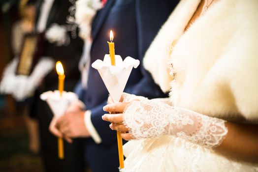 Wedding ceremony in orthodox church. Bride and groom holding the candles. Close up.