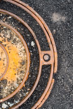 Rusty metal manhole cover in black asphalt surface