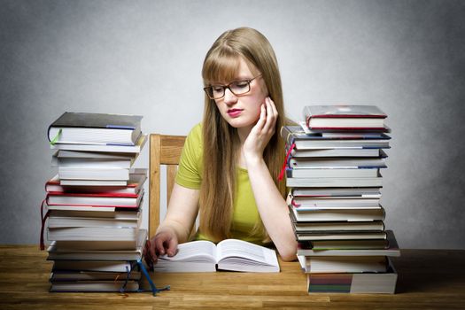 young woman with lots of books at a table is reading bored book