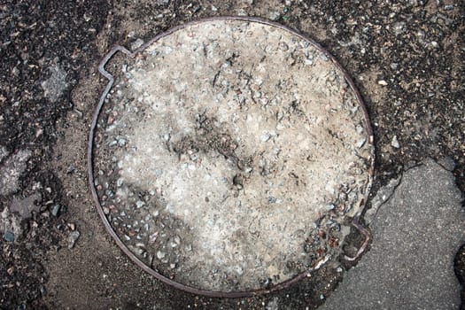 Manhole with the metal cover surface paved with asphalt.