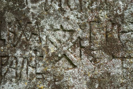 Moss-grown surface of the old stone cross with engraved Old Church Slavonic inscriptions. Kyiv, Ukraine. Close up.