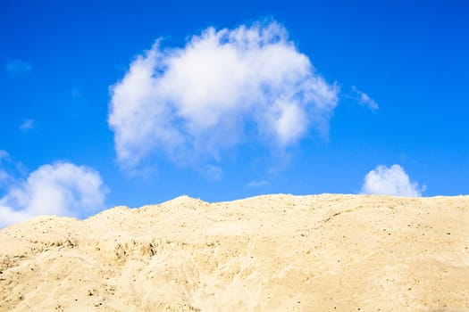 Pile of sand and blue sky with white clouds over it.