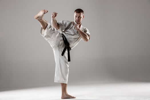 Man in white kimono and black belt training karate over gray background.