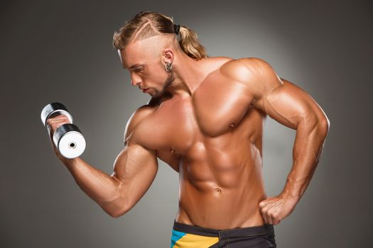 torso of attractive male body builder with dumbbell on gray background.