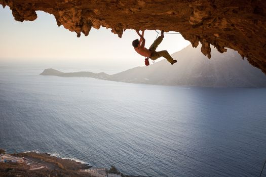 Rock climber climbing along a roof in a cave at sunset