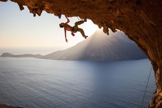 Rock climber climbing along a roof in cave at sunset