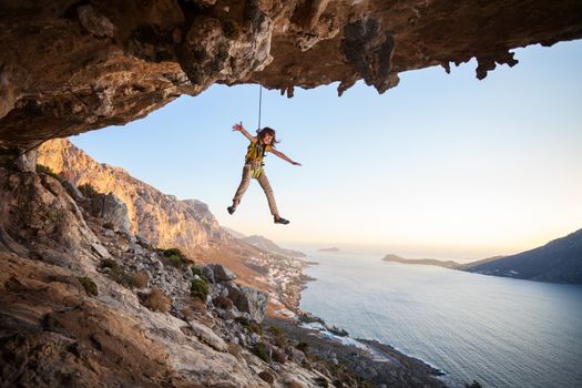 Seven-year old girl hanging on rope while lead climbing at sunset