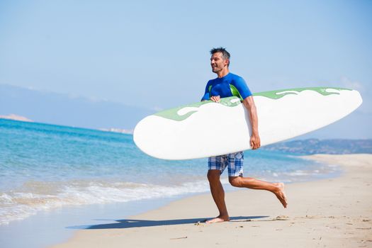 Strong young surf man runing at the beach with a surfboard.