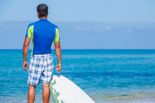 Strong young surf man with a surfboard watching at the sea.