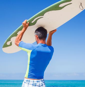 Back view of strong young surf man at the beach with a surfboard.