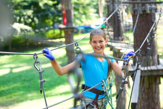 Portrait of happy school girl enjoying activity in a climbing adventure park on a summer day