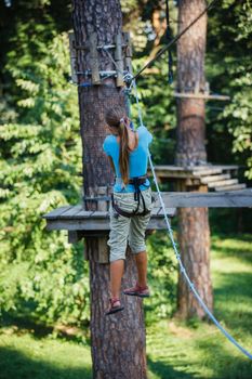 Back view of happy school girl enjoying activity in a climbing adventure park on a summer day
