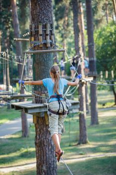 Back view of happy school girl enjoying activity in a climbing adventure park on a summer day