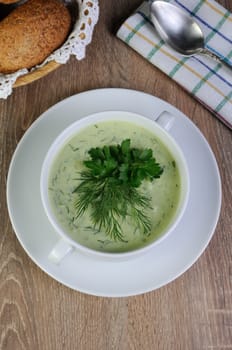 A bowl of soup with dill sauce and parsley on the table with croutons