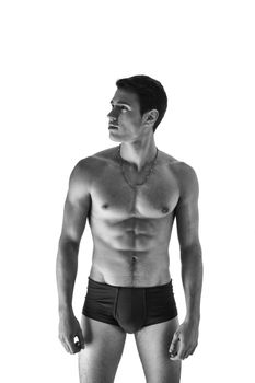 Black and white shot or handsome, fit young man wearing only underwear standing isolated on white background, looking to the left