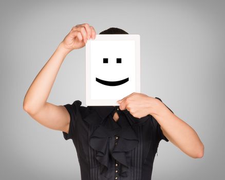 Girl in black dress covered her face with tablet. On screen code smiley. Gray background