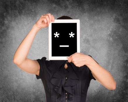 Girl in black dress covered her face with tablet. On screen code smiley. Concrete background