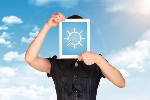 Girl in dress covered her face with tablet. On screen sun symbol. Blue sky with clouds as backdrop