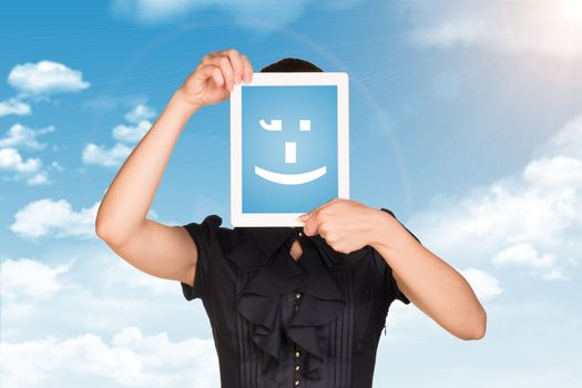 Girl in black dress covered her face with tablet. On screen code smiley. Blue sky with clouds as backdrop