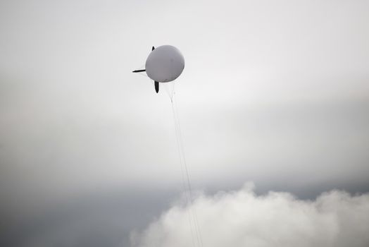 single white blimp high in the grey sky