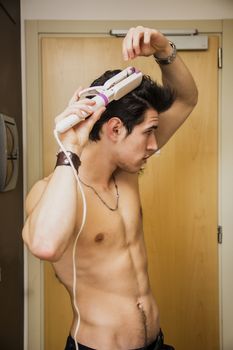 Shirtless Handsome Young Man Ironing his Short Hair in his Room While Looking to a Side