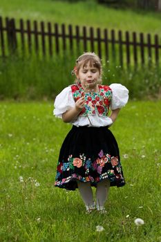 Little girl dressed in traditional costume, blowing to dandelion