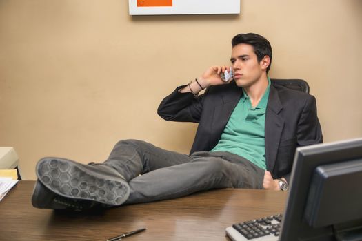 Successful handsome young businessman sitting at his desk in the office talking on phone