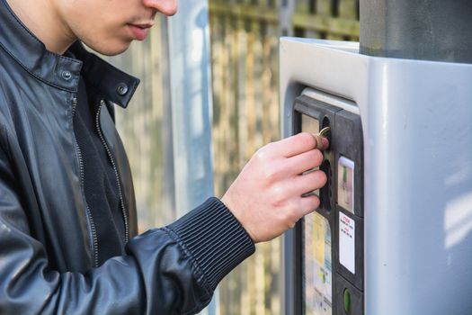 Close up of young man paying and waiting for a parking ticket to be dispensed from the ticket booth at the side of a street