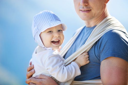 Happy toddler boy in sling, father carrying son outdoors