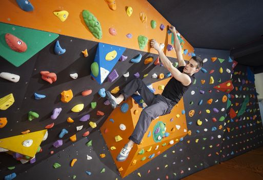 Young man practicing bouldering in indoor climbing gym