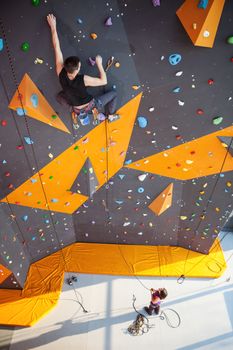 Young man practicing rock-climbing on a rock wall indoors