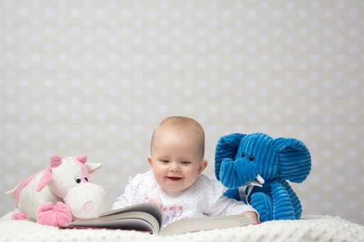 Smiling baby girl reading a book with little toy friends