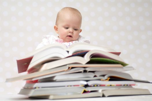 Cute baby girl sitting behind a pile of books