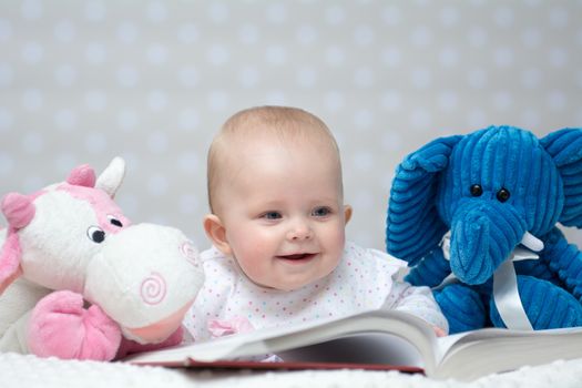 Happy baby girl reading a book with little toy friends
