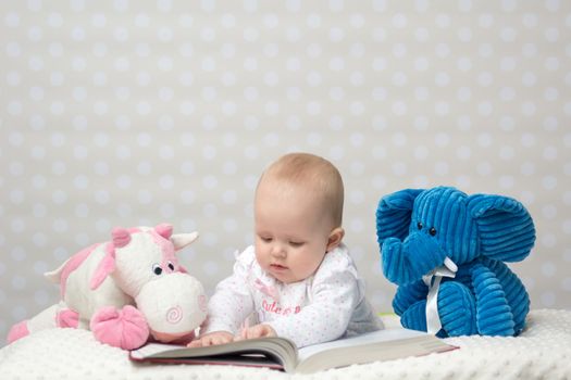 Baby girl reading a book with little toy friends