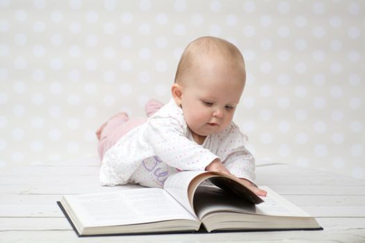 Baby girl lying on the belly reading a book